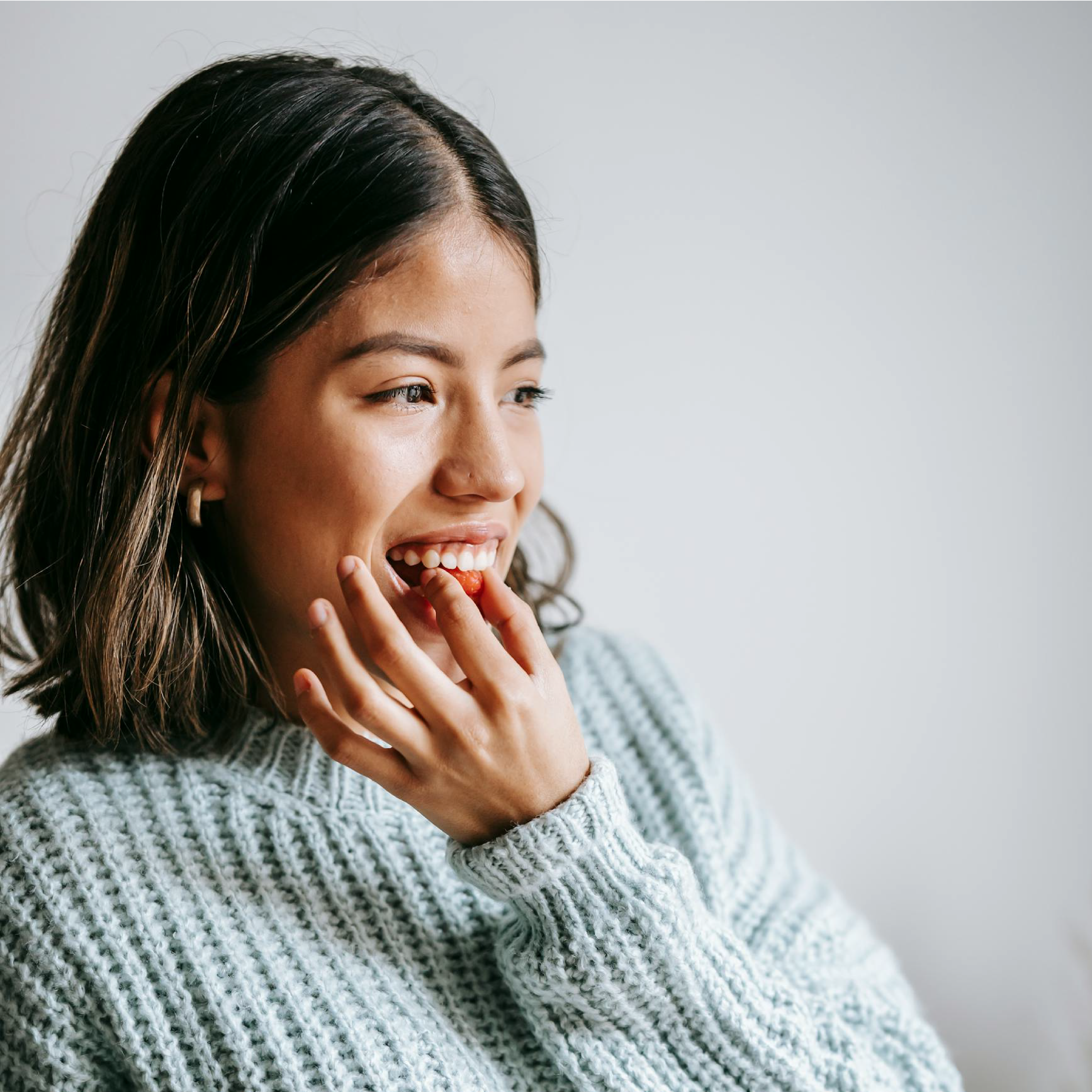 Woman wearing a light blue sweater eating sbt gummies