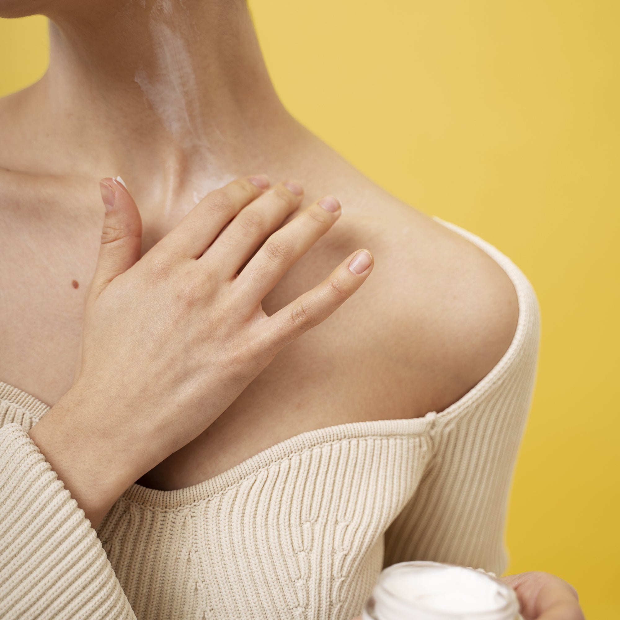 A beautiful young woman applying cream to shoulder against a yellow background