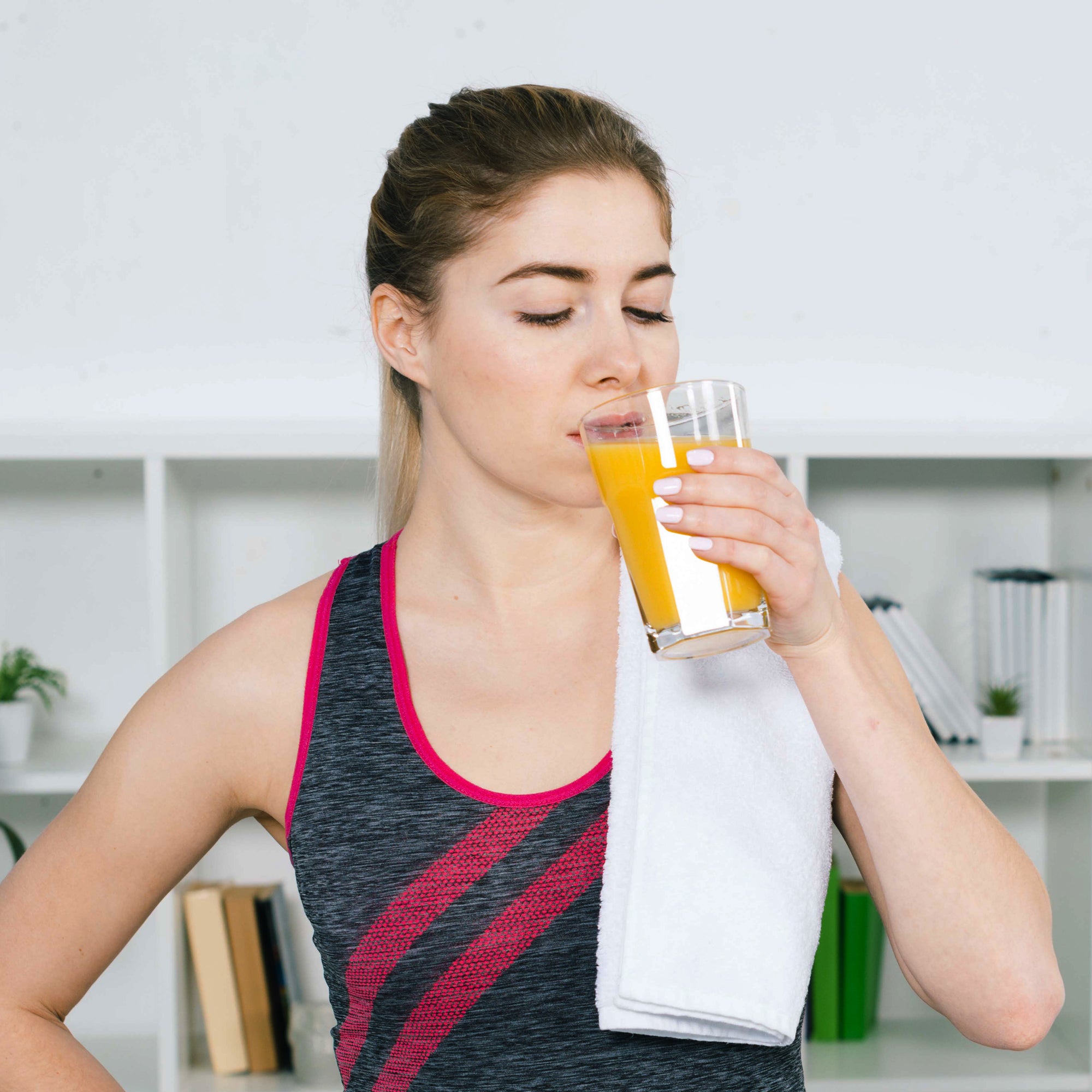 Woman drinking wellwith fitwell juice after a workout with a white towel draped over her shoulder.
