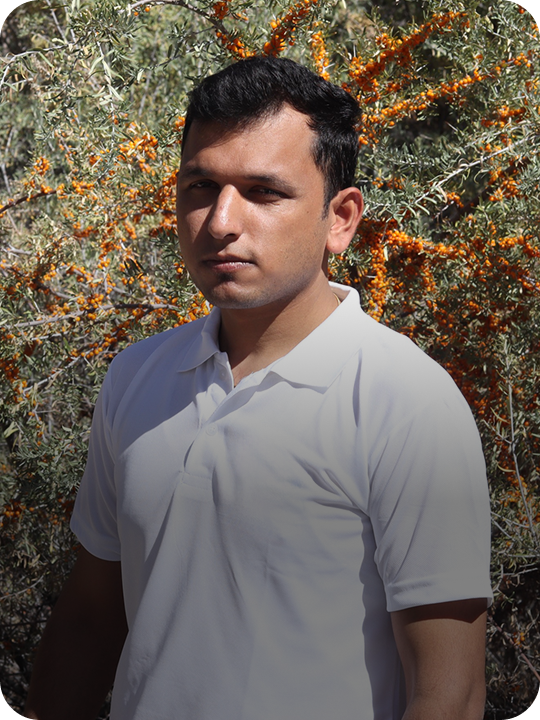 Udit Chawla director of wellwith wearing a white polo tshirt standing in front of a bush with sea buckthorn berries.